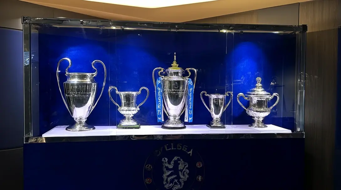 Vetrina con cinque trofei d'argento, tra cui la Champions League con le orecchie grandi, su sfondo blu sopra lo stemma del Chelsea.