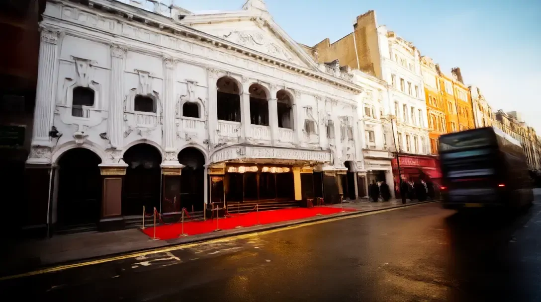 The London Palladium frontage at dusk with a red carpet leading to the entrance and a bus passing