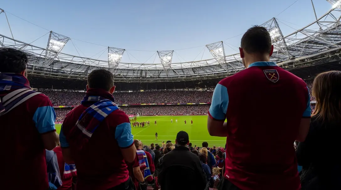 West Ham fans in claret and sky-blue shirts and scarves watch from the stands at London Stadium, roof and floodlight masts above.